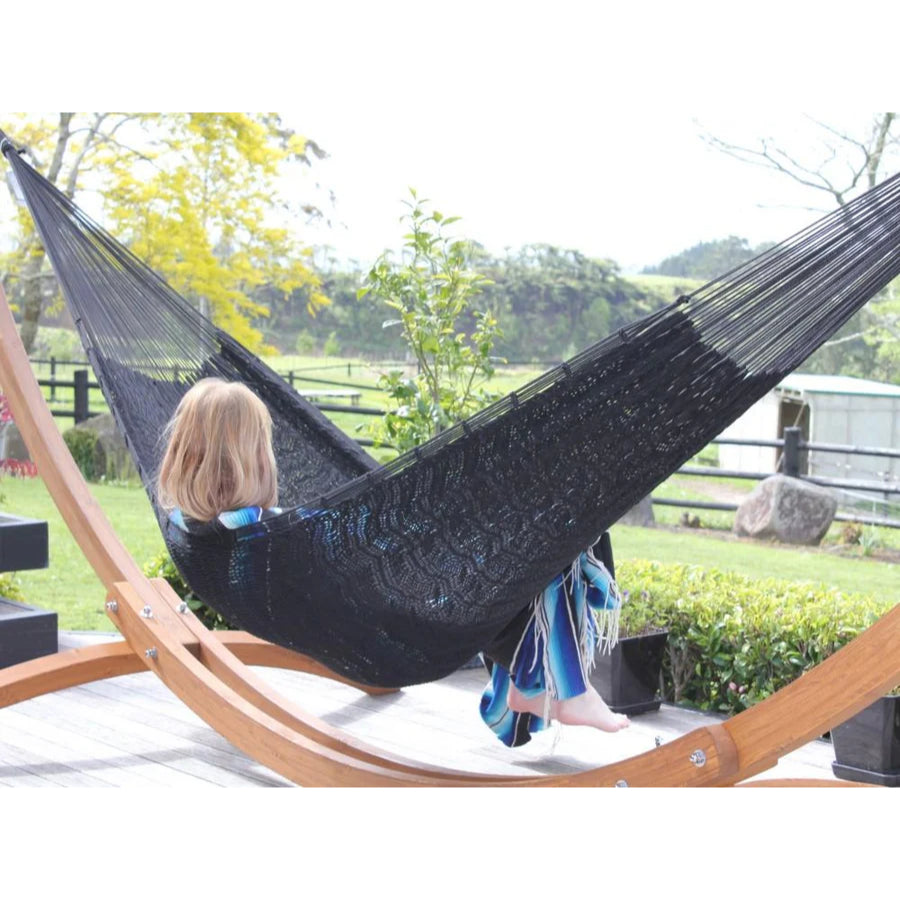 Person relaxing in a black hammock with wooden stand outdoors.