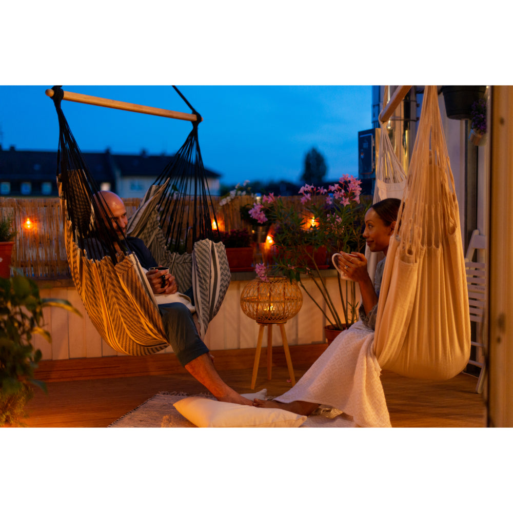 couple relaxing outdoors with warm drinks at night time in hammock chairs