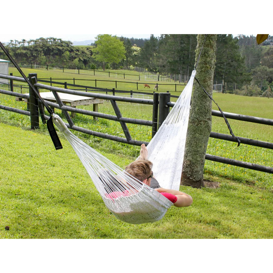 Person relaxing in a white hammock outdoors with greenery in the background