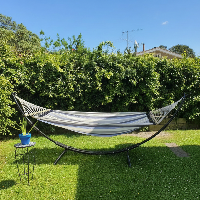 Curved black metal stand with blue and white hammock hanging from in it lush green garden.
