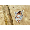 Woman reading a book in a hammock chair hung from a tree at the beach