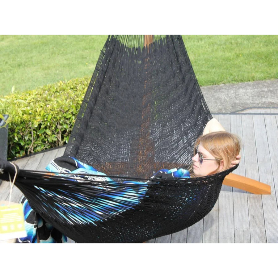 Person relaxing in a black hammock with colourful blanket on a wooden deck.