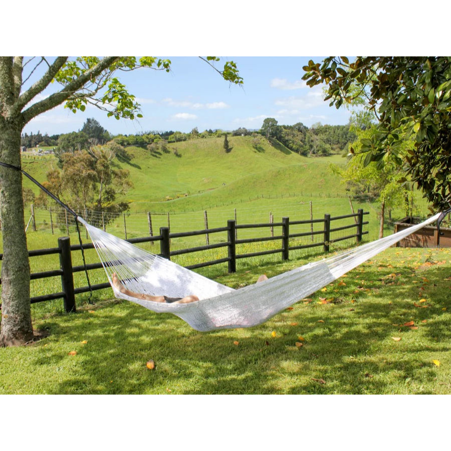 Large white Mexican hammock hung from trees overlooking farmland