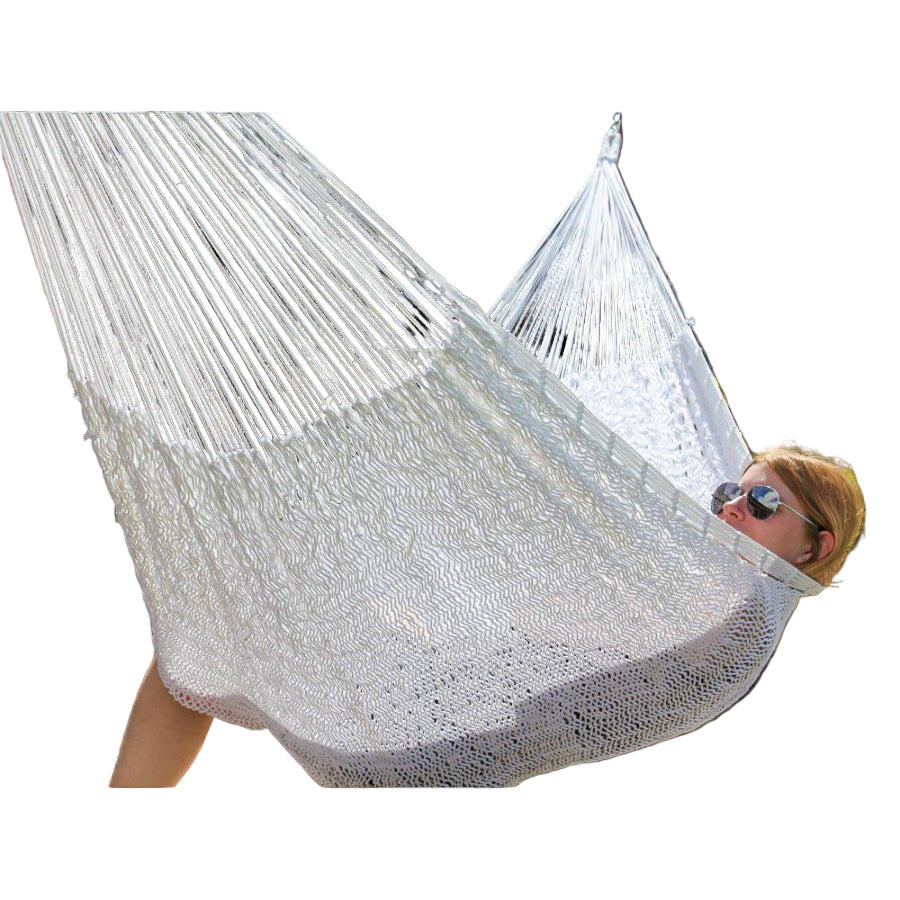 Person relaxing in a white hammock outdoors with greenery in the background